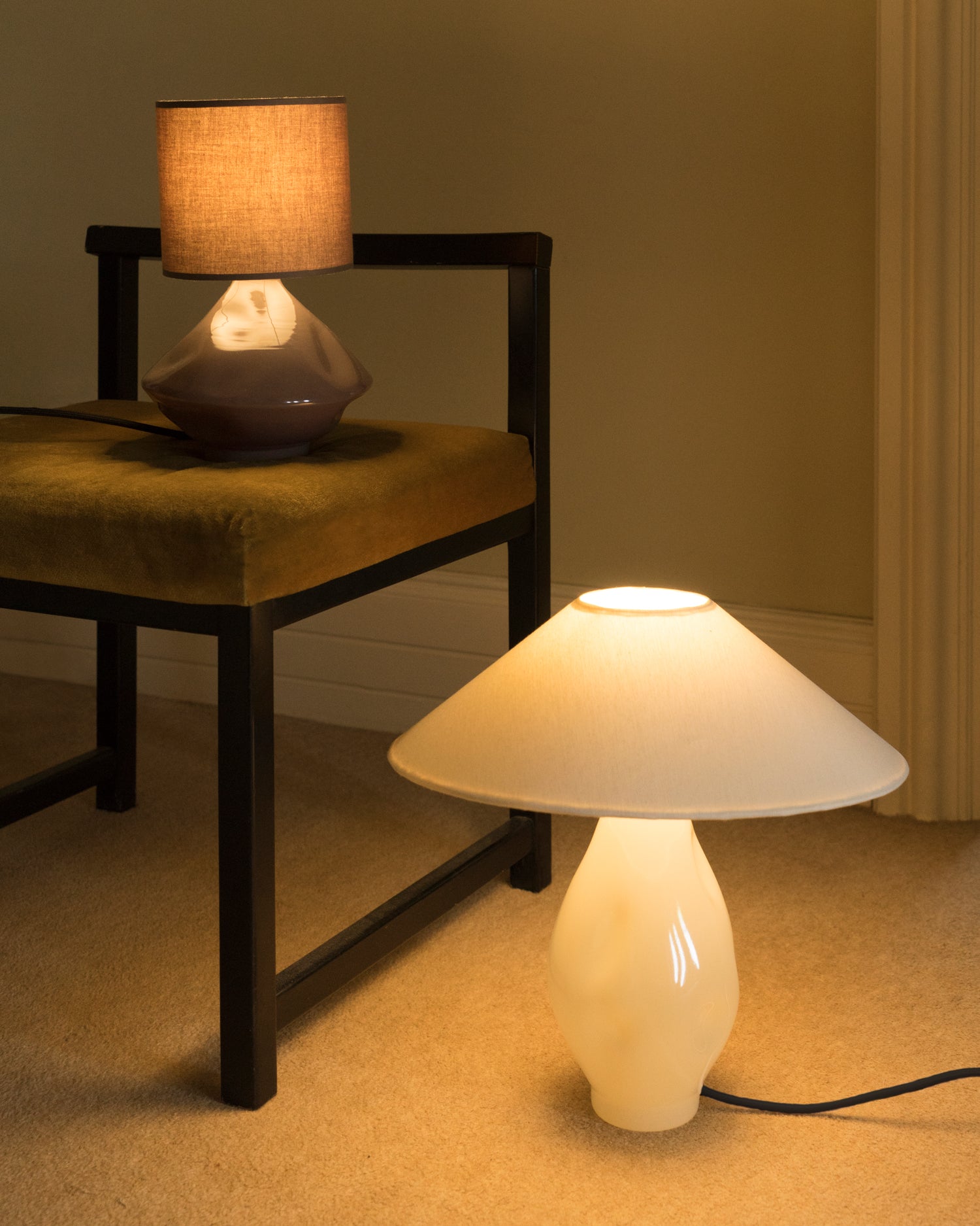 Beige glass table lamp with warm conical shade shown on floor next to chair and linen drum lamp
