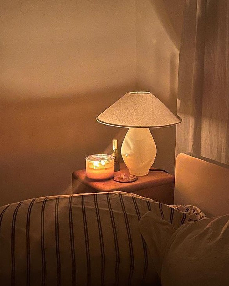 Beige glass table lamp with oversized conical shade styled on wood nightstand with candle