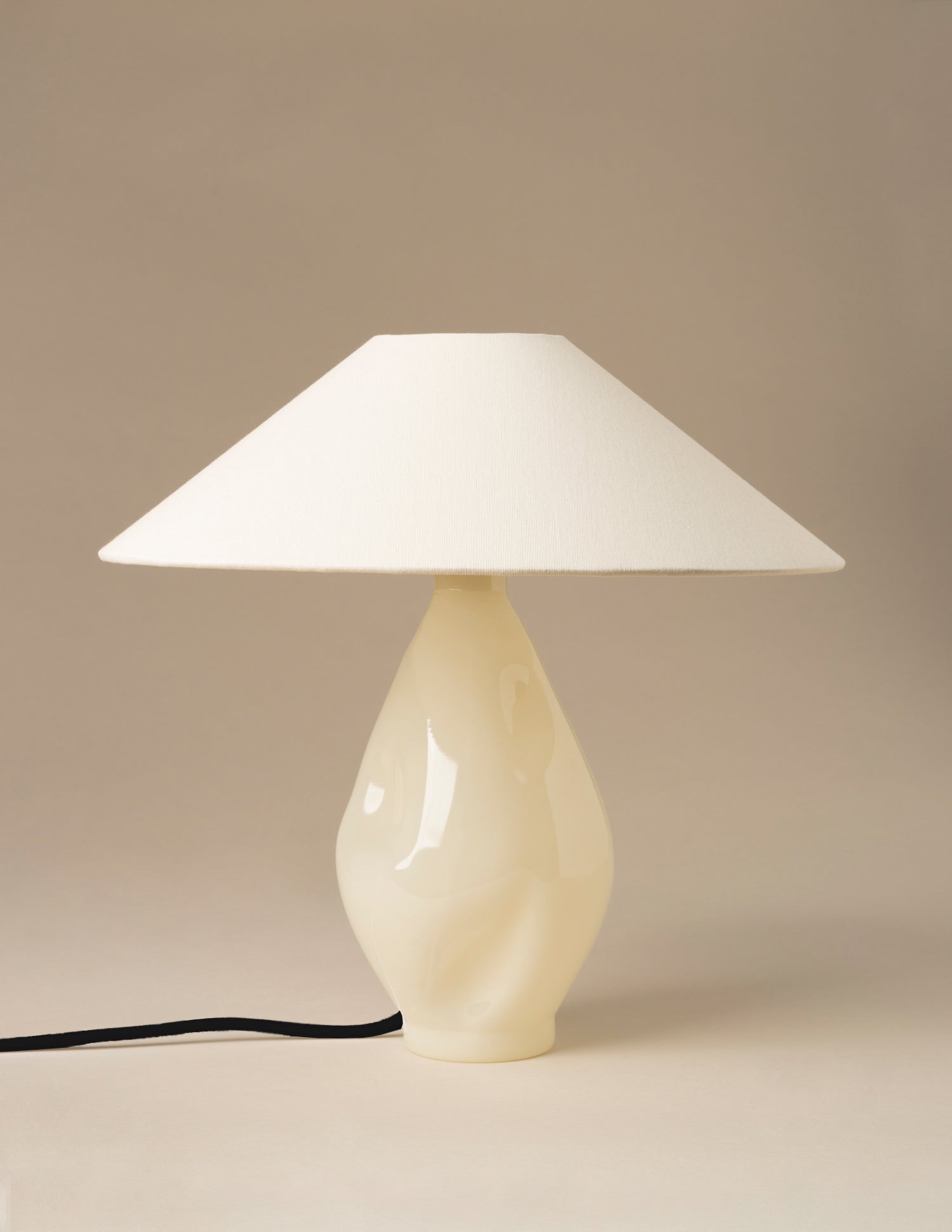 Studio shot of beige glass table lamp with bulbous base and wide conical canvas lampshade