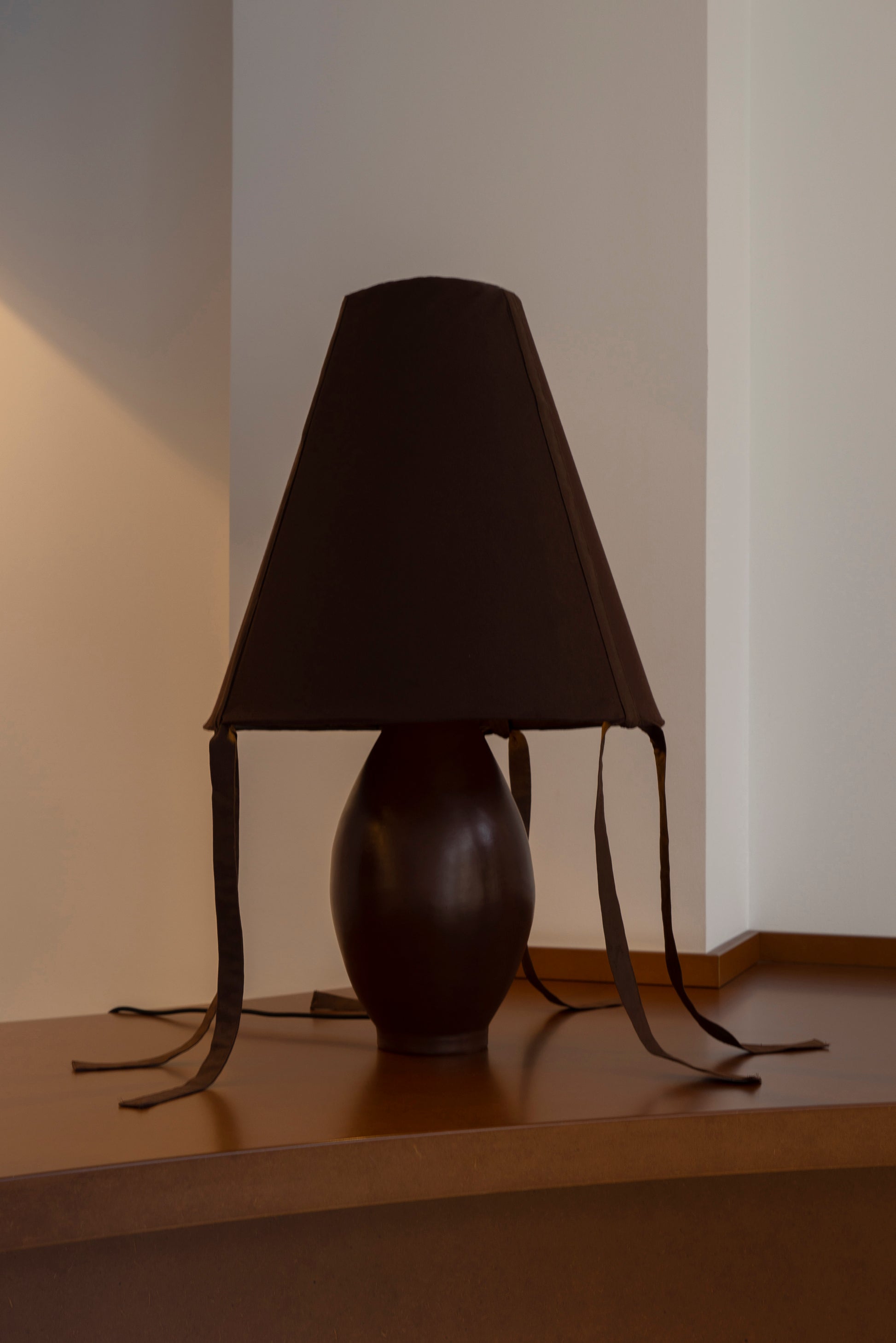 Brown ceramic table lamp with cotton shade and bow details styled on wood console against neutral wall