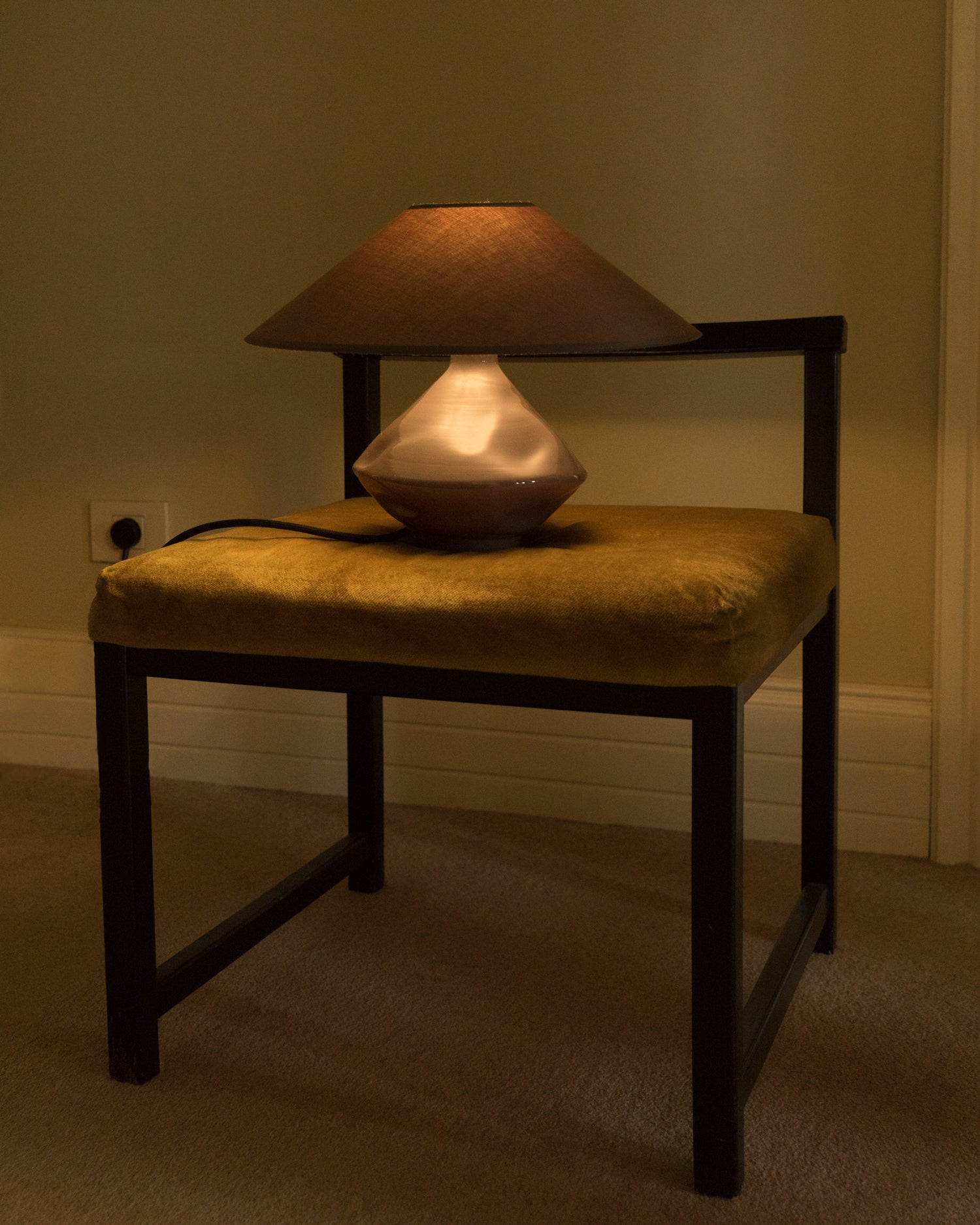 Brown glass lamp glowing softly on vintage velvet chair, casting warm ambient light