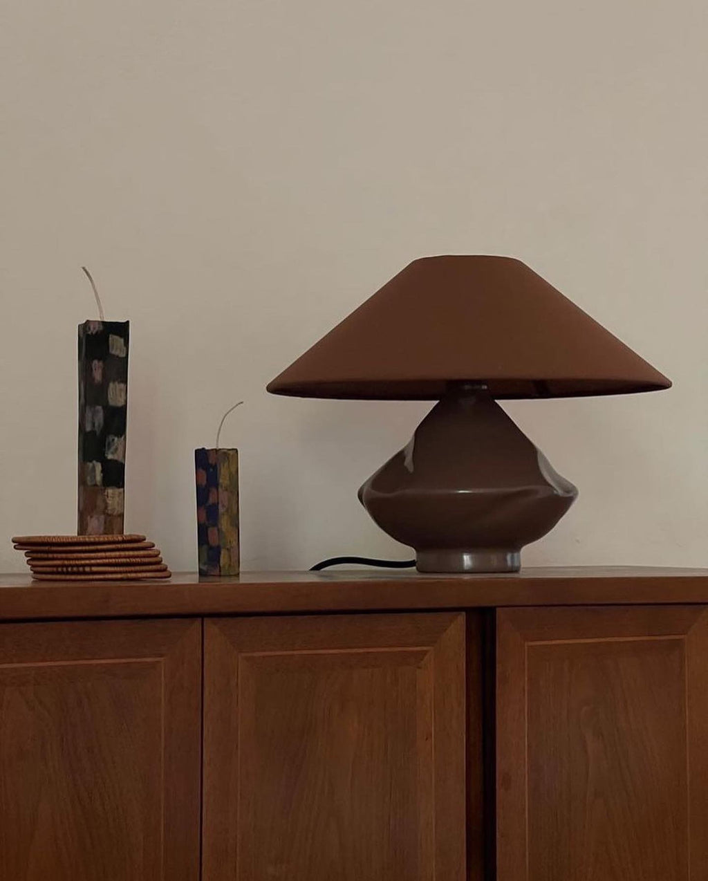Brown glass table lamp with conical shade styled on mid-century cabinet with sculptural candles