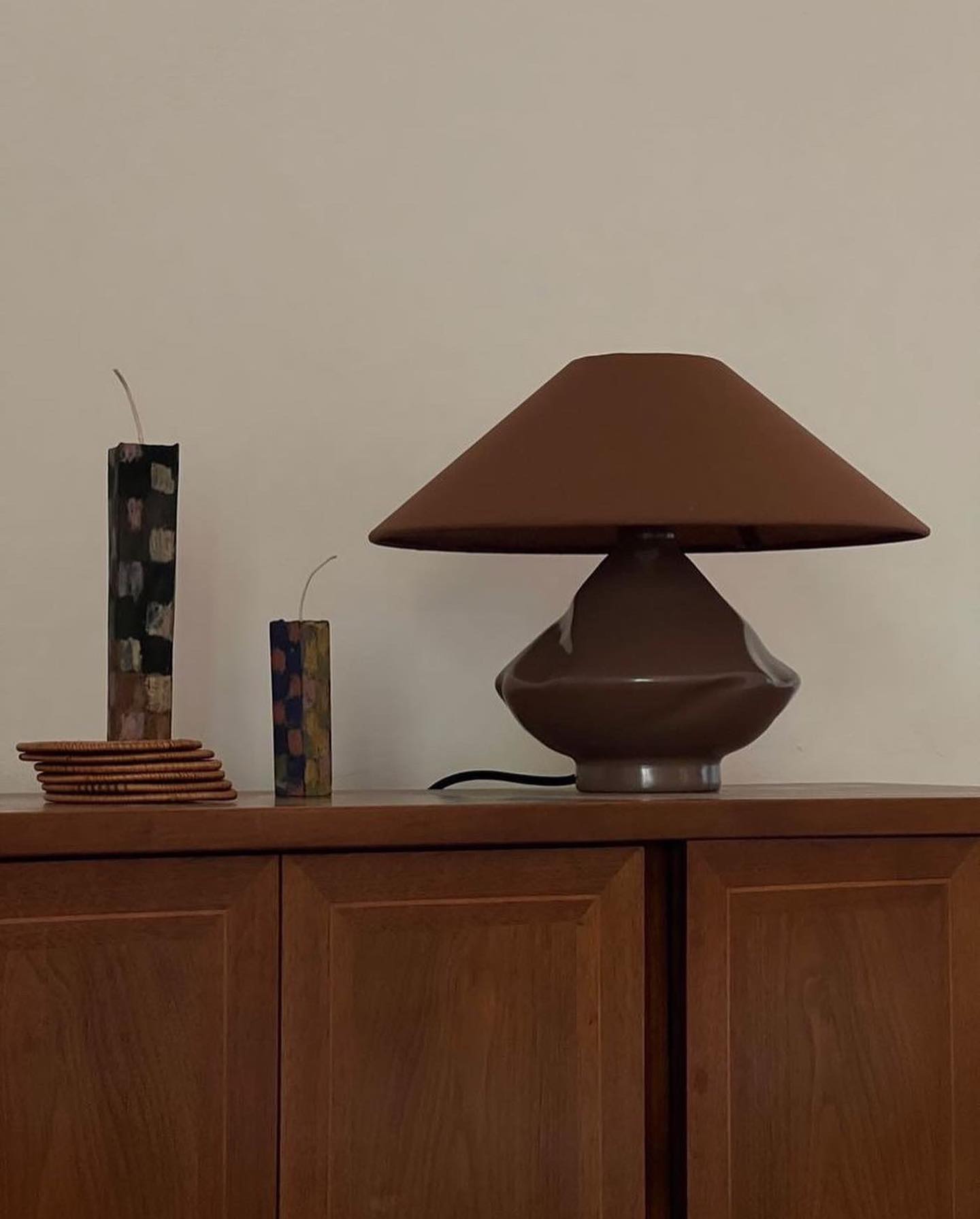 Brown glass table lamp with conical shade styled on mid-century cabinet with sculptural candles