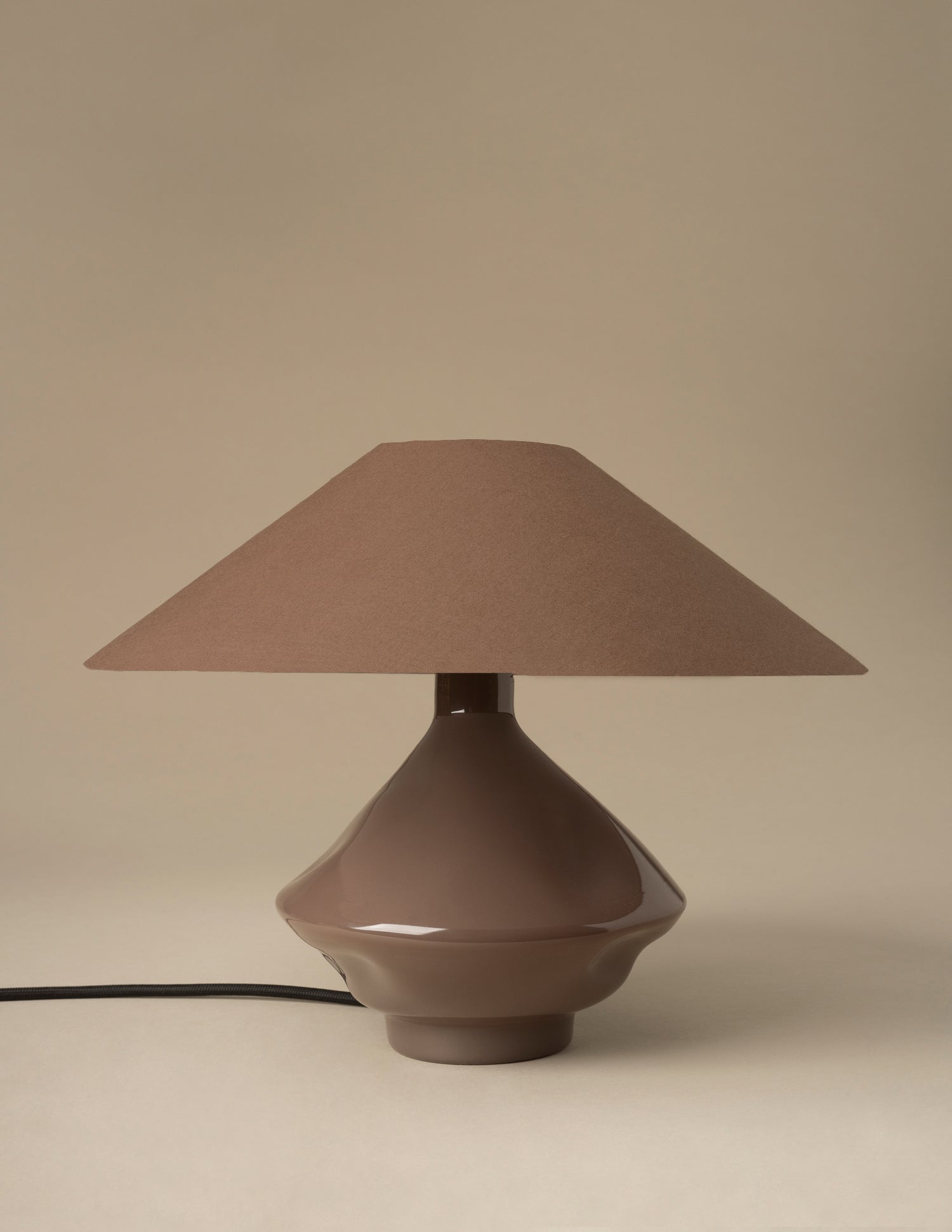 Brown glass lamp with oversized conical fabric shade on neutral studio backdrop