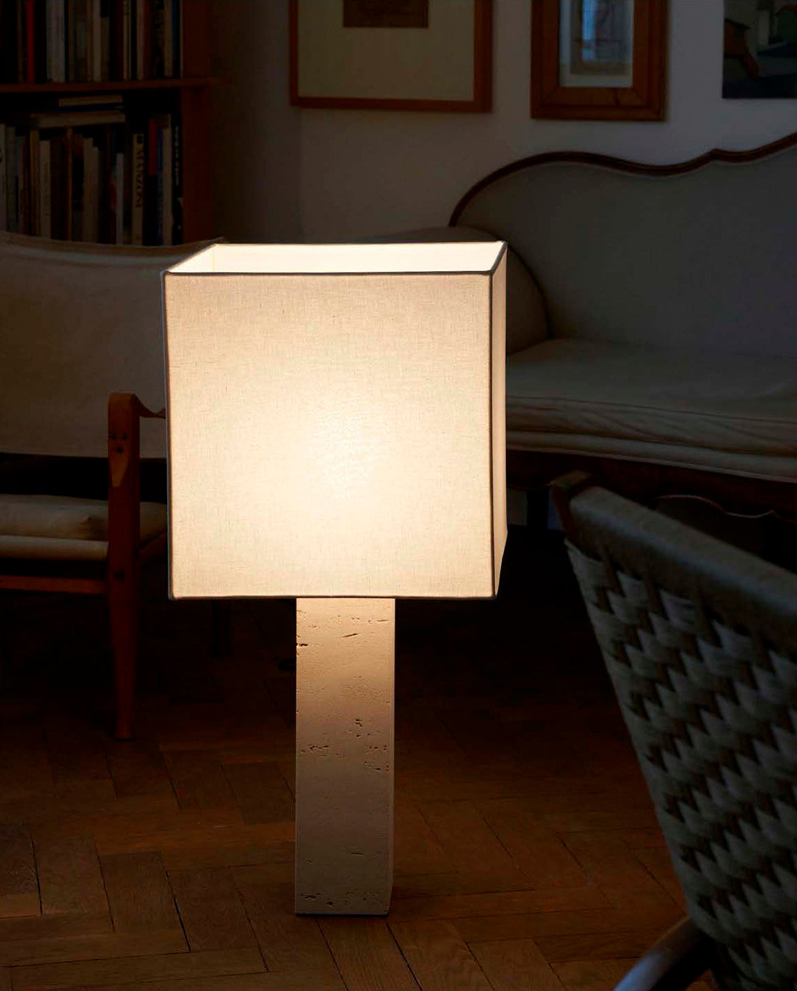Table lamp with a square white linen shade and square white travertine base on a herringbone wood floor