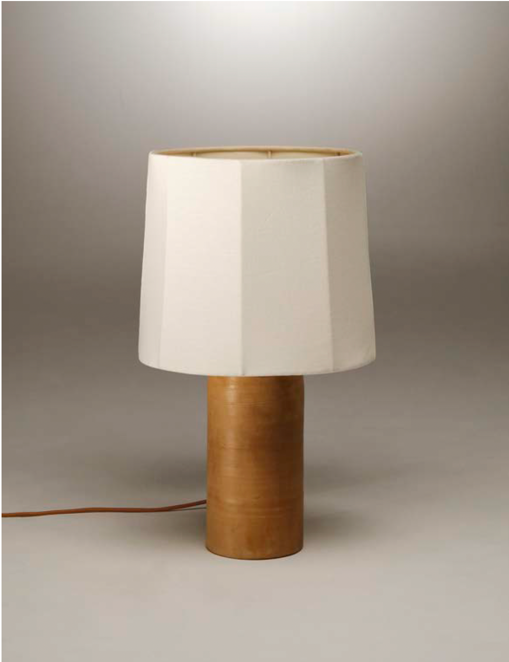 Table lamp with a fluted white linen shade on a terracotta rounded base against a gray background